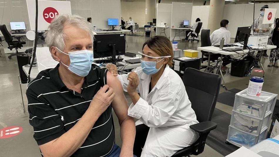 Renaud Gagné wears a mask while receiving a vaccination from a health care worker in a mask and faceshield. 